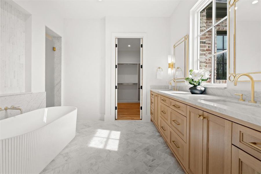 Full bathroom featuring double vanity, a freestanding tub, a spacious closet, and a sink