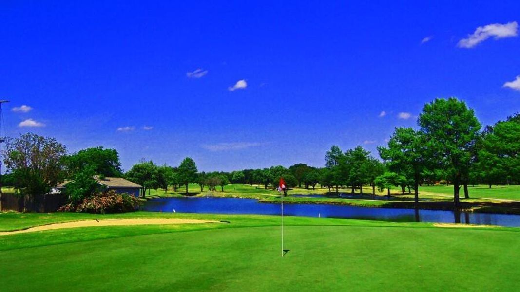 View of community featuring a water view, a lawn, view of golf course, a putting green, and view of scattered trees View of community featuring a water view, a lawn, view of golf course, a putting green, and view of scattered trees