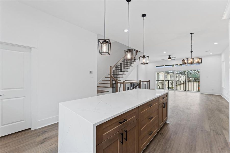 This open-concept home features a modern kitchen island with pendant lighting, a spacious living area, and large windows for natural light. The staircase adds elegance, and the sliding doors lead to an outdoor view.