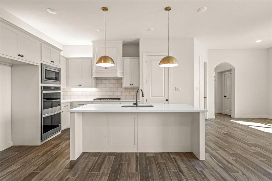Kitchen featuring a sink, appliances with stainless steel finishes, dark wood-type flooring, tasteful backsplash, and light countertops