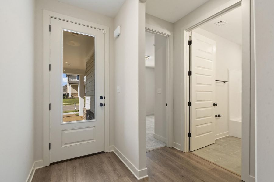 Wood-finish flooring throughout, white interior walls, full-light entry door, bathroom with a white tub and tiled floor, and a paneled interior door Wood-finish flooring throughout, white interior walls, full-light entry door, bathroom with a white tub and tiled floor, and a paneled interior door