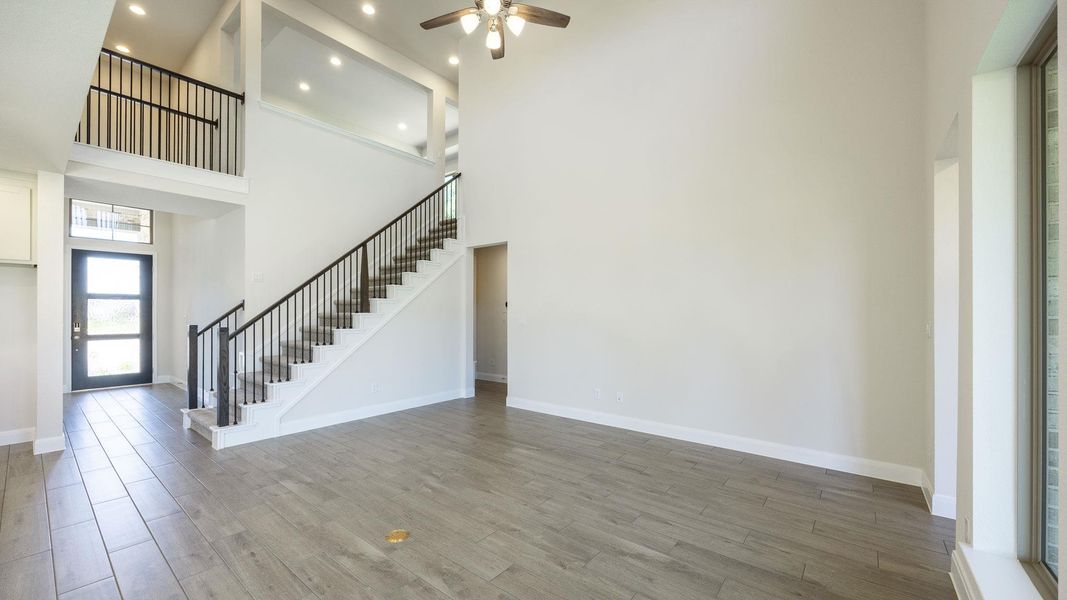 Unfurnished living room with wood finished floors, stairs, a high ceiling, and a ceiling fan Unfurnished living room with wood finished floors, stairs, a high ceiling, and a ceiling fan