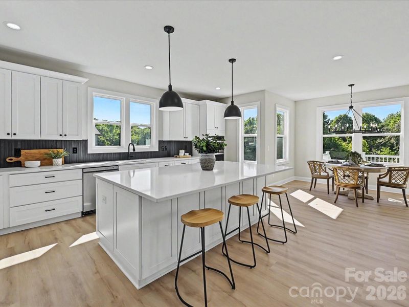 Bright designer kitchen features a large quartz island, stainless steel appliances, double ovens, abundant cabinetry, and an open-concept layout perfect for everyday living and entertaining.