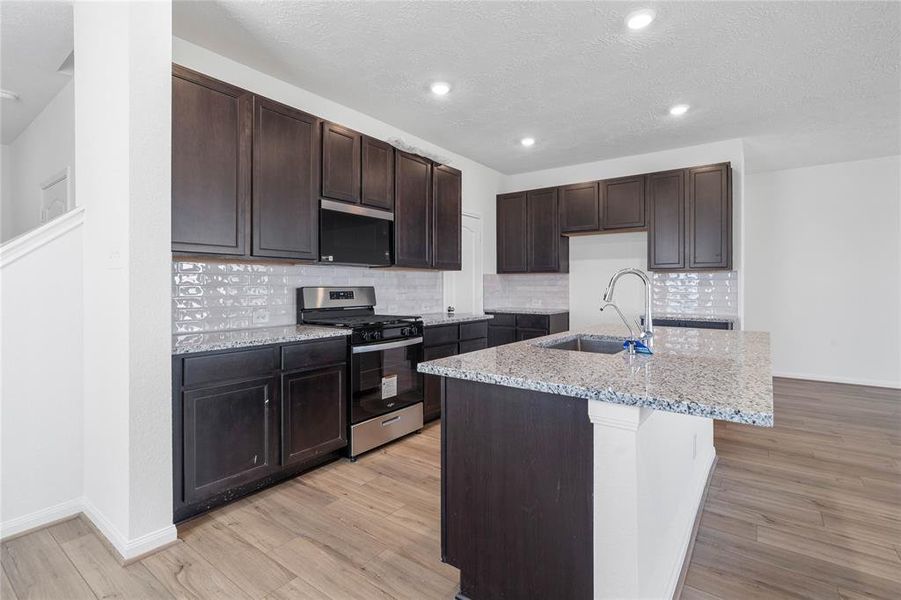 This spacious kitchen features high ceilings, stained wood cabinets, granite countertops, SS appliances, modern tile backsplash, recessed lighting, huge granite kitchen island with sink and space for breakfast bar, and a pantry all overlooking your huge family room.