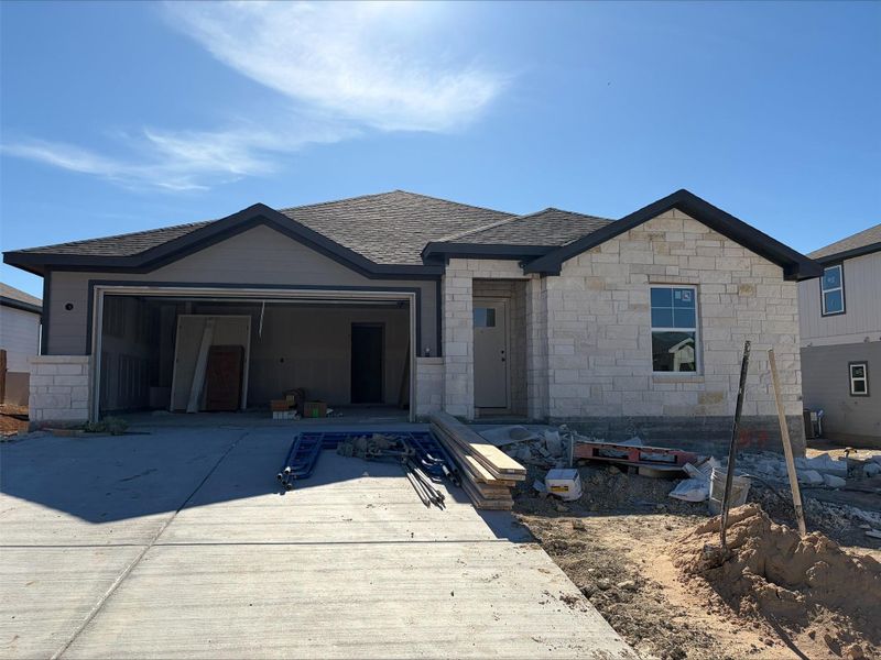 View of front of property with stone siding, driveway, a garage, and a patio