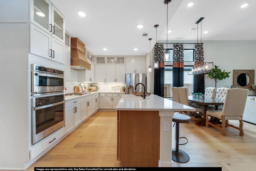 Kitchen with glass insert cabinets, pendant lighting, white cabinets, a center island with sink, and light wood-type flooring Kitchen with glass insert cabinets, pendant lighting, white cabinets, a center island with sink, and light wood-type flooring