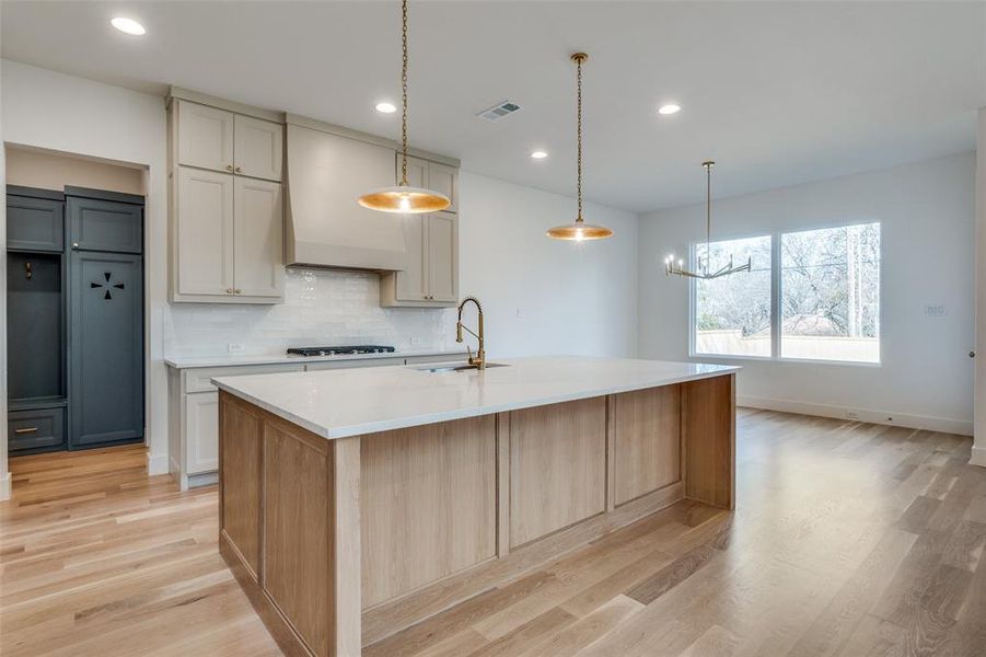 Kitchen featuring pendant lighting, sink, an island with sink, and custom exhaust hood