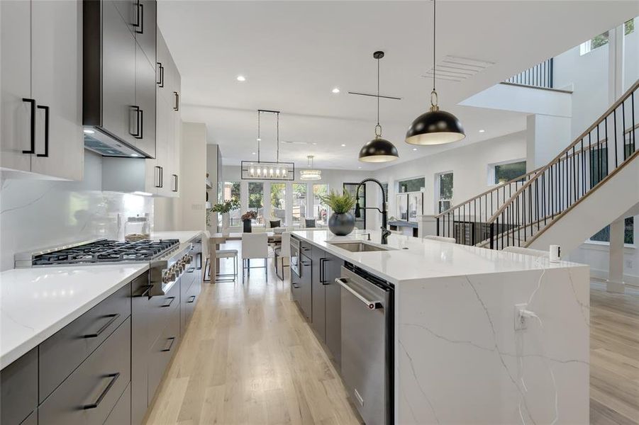 Kitchen with a spacious island, hanging light fixtures, appliances with stainless steel finishes, and gray cabinetry