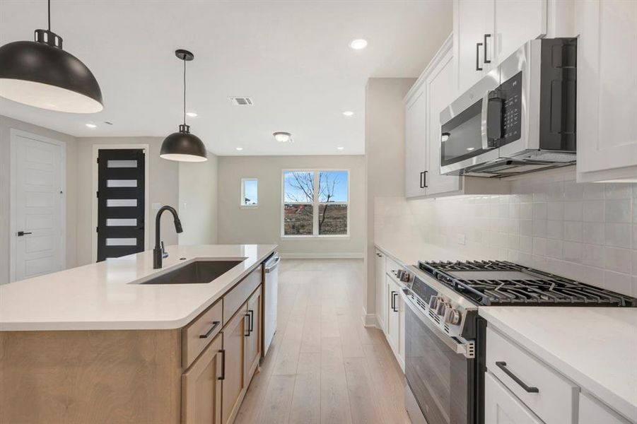 Kitchen featuring stainless steel appliances, white cabinetry, hanging light fixtures, an island with sink, and light wood finished floors