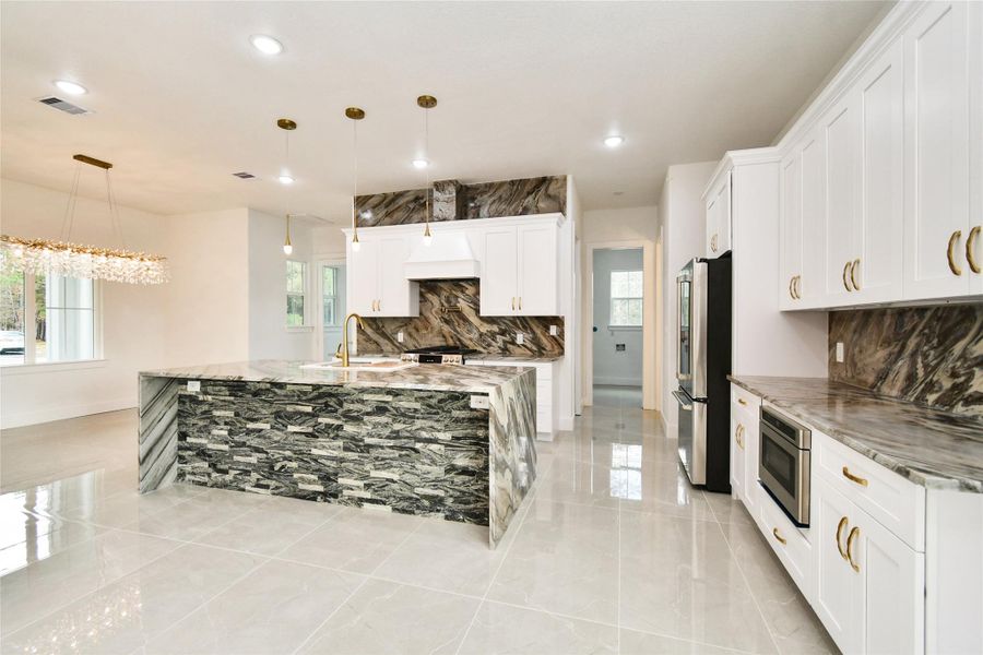 The entertainer’s kitchen features a unique waterfall-edge island with stacked stone accents, perfectly complemented by the dramatic book-matched stone backsplashes and professional-grade appliances.