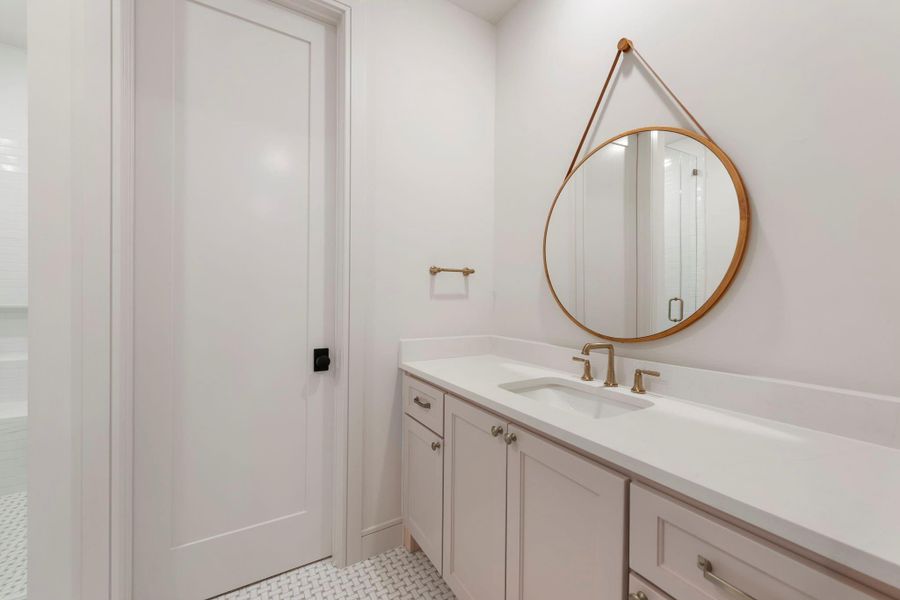 Stylish secondary bathroom featuring a sleek vanity with stone countertops, designer fixtures, and a round statement mirror creating a clean, modern aesthetic.
