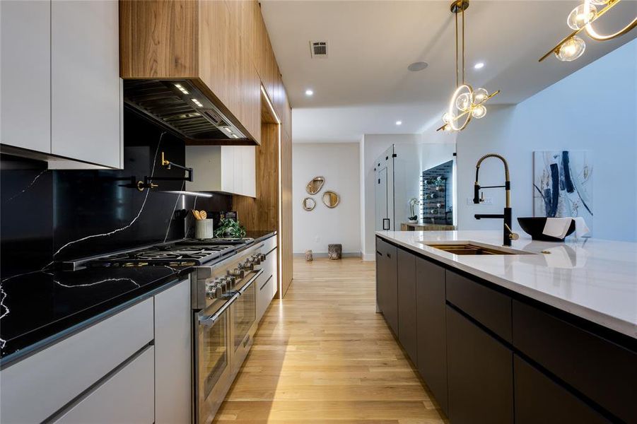 Kitchen featuring backsplash, dark stone counters, light hardwood / wood-style flooring, high end stainless steel range oven, and decorative light fixtures