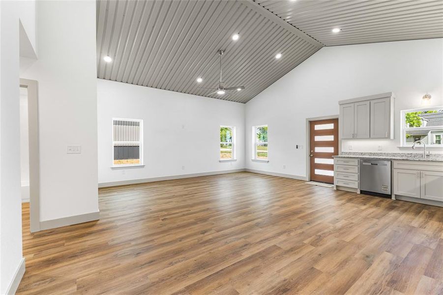 Unfurnished living room featuring high vaulted ceiling, healthy amount of natural light, light wood-type flooring, baseboards, and recessed lighting Unfurnished living room featuring high vaulted ceiling, healthy amount of natural light, light wood-type flooring, baseboards, and recessed lighting