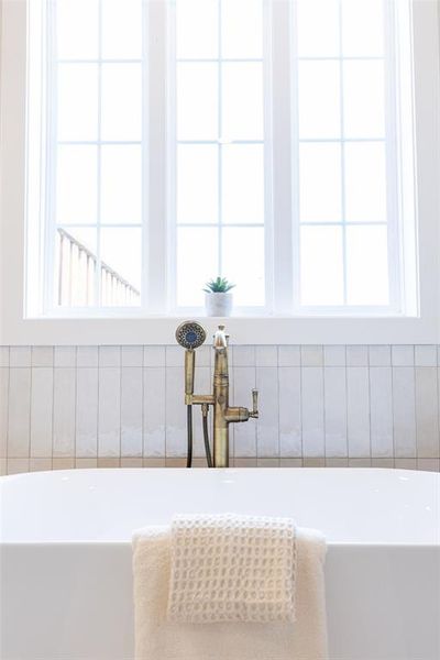 Freestanding soaking tub with a floor-mounted brass faucet and handheld shower sprayer