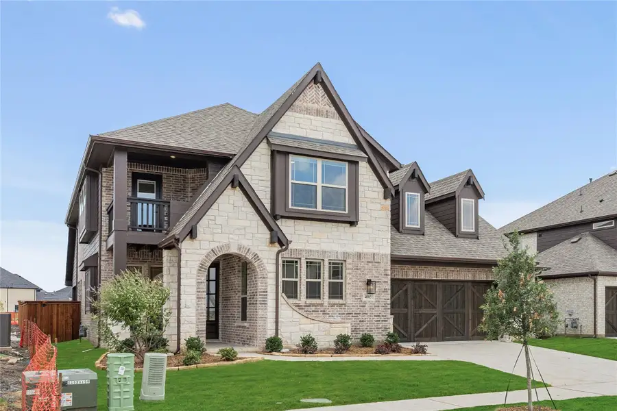 Two-story home with stone and brick exterior, arched entry, second-floor balcony, and two-car garage