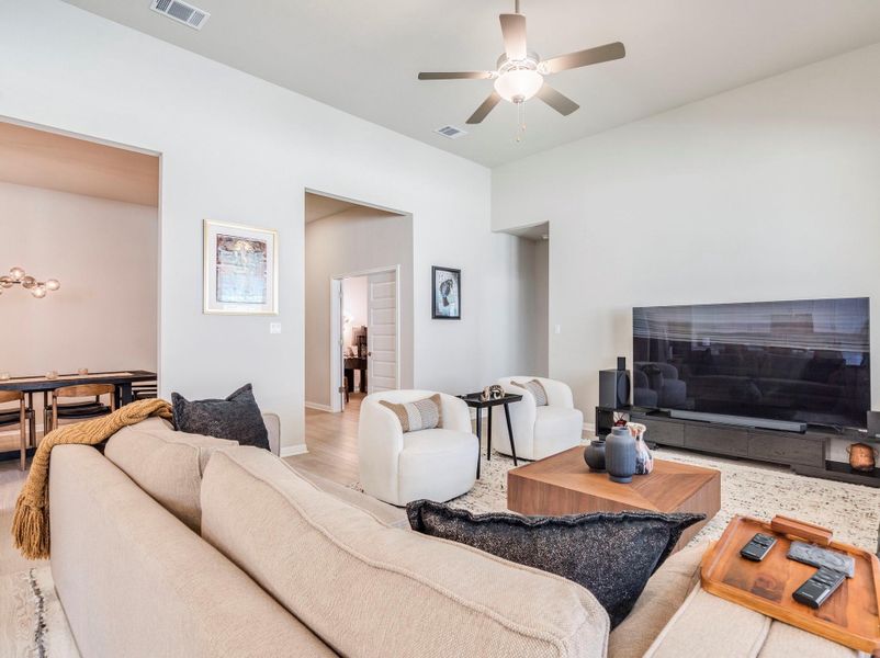The naturally illuminated living room features a ceiling fan, light-colored walls, and wood flooring.