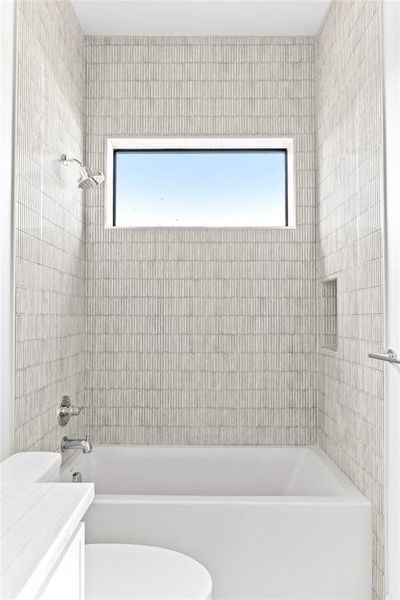 Bathroom featuring a white bathtub, chrome shower fixtures, and textured subway tile surround
