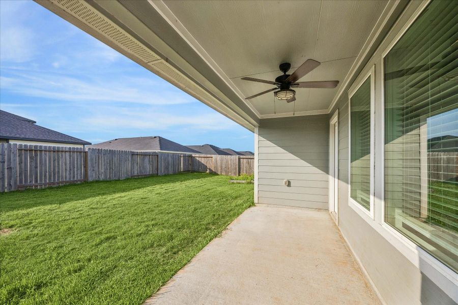 Spacious backyard with a well-maintained lawn, enclosed by a wooden fence. The covered patio features a ceiling fan, providing a comfortable outdoor space.