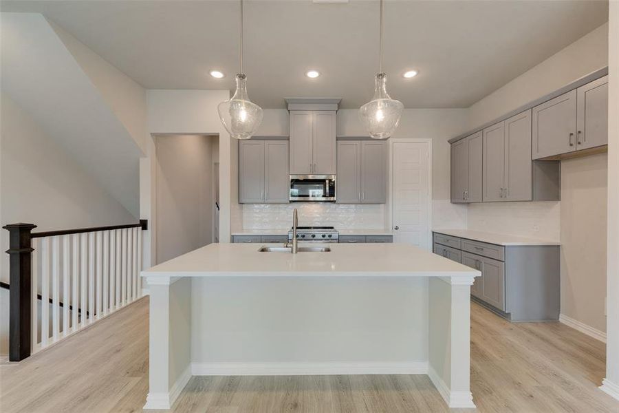 Kitchen with tasteful backsplash, light wood-type flooring, sink, a center island with sink, and gray cabinetry