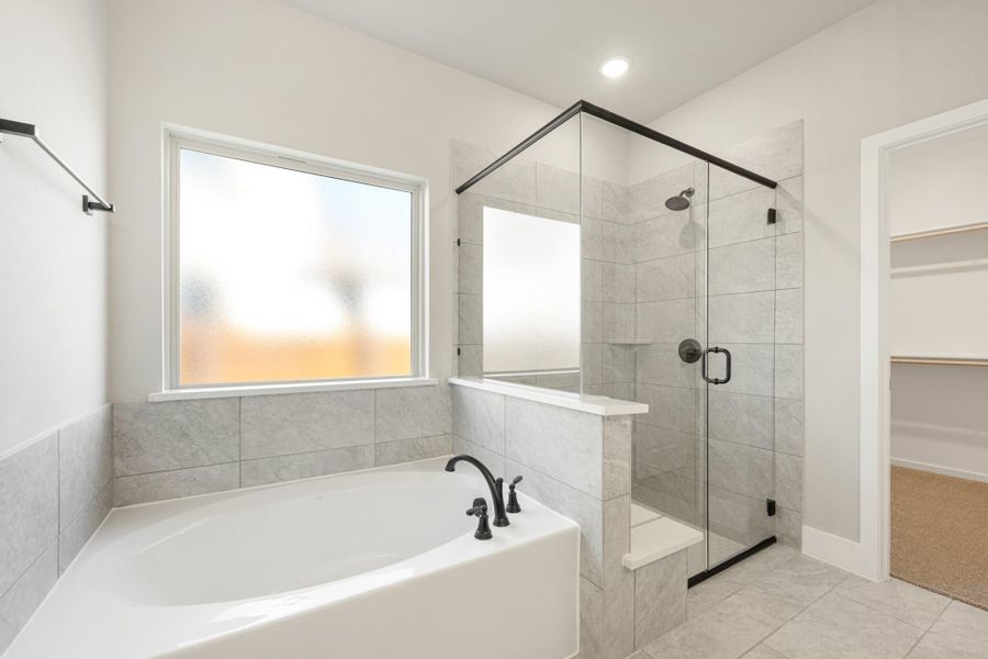 Master bathroom with soaking tub, glass walk-in shower, gray tile walls, and access to walk-in closet