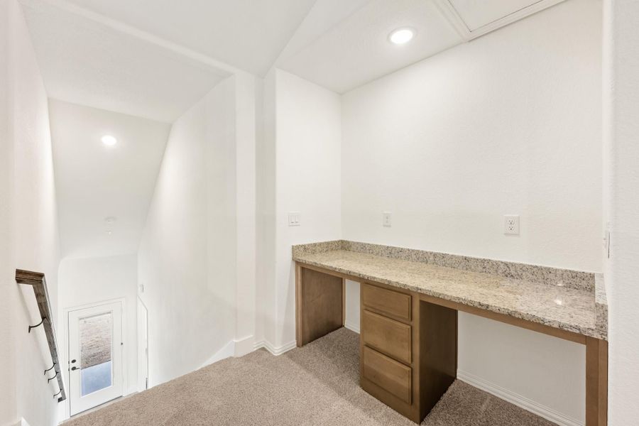 Built-in desk with granite countertop and wood drawers on carpet flooring near staircase landing Built-in desk with granite countertop and wood drawers on carpet flooring near staircase landing