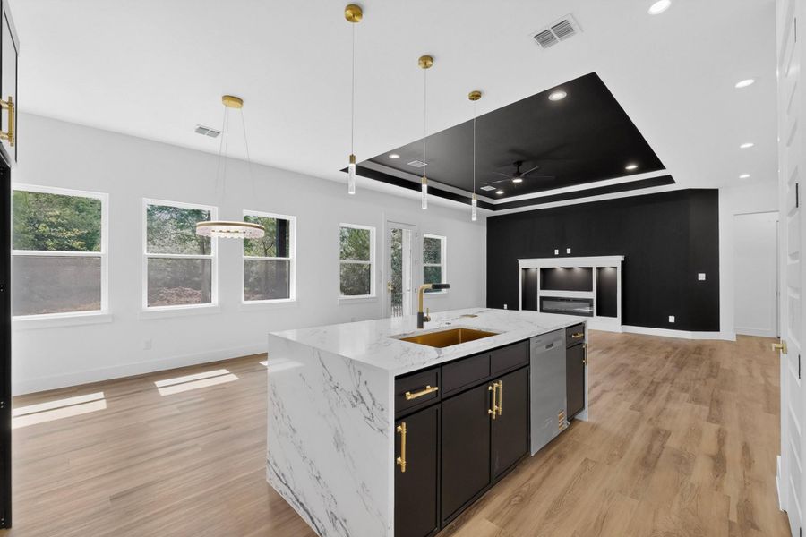 A sleek island with a gold sink and white countertops anchors this spacious open concept living area.