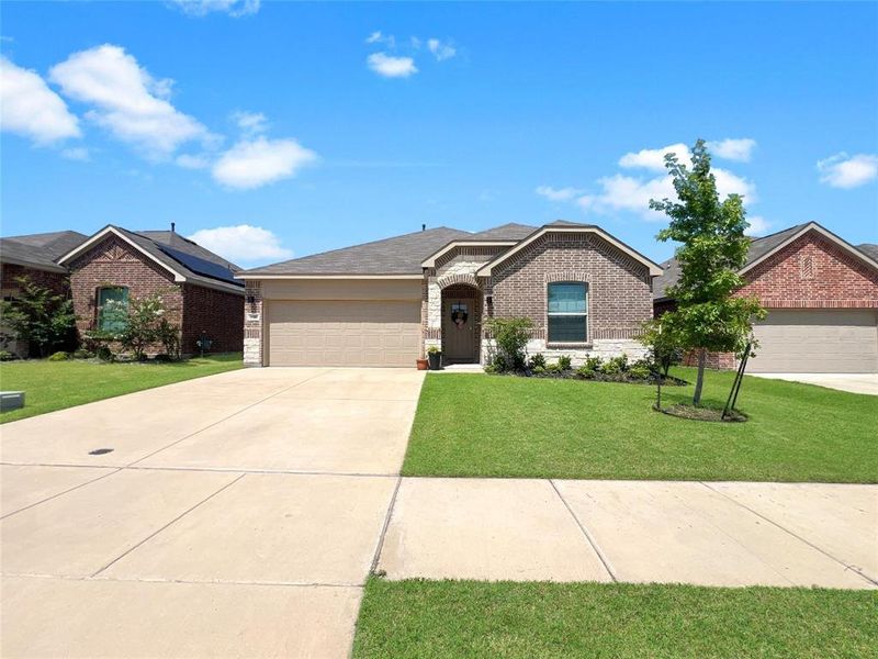 Ranch-style house featuring brick siding, an attached garage, a front lawn, concrete driveway, and stone siding