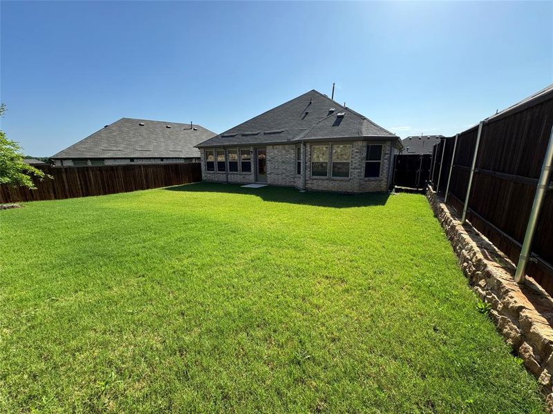 Expansive backyard featuring a manicured lawn, full privacy fencing, and a stone retaining wall Expansive backyard featuring a manicured lawn, full privacy fencing, and a stone retaining wall