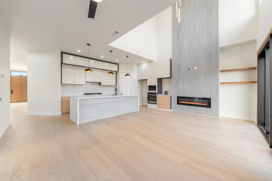 Unfurnished living room featuring light wood-type flooring, a large fireplace, a towering ceiling, recessed lighting, and a ceiling fan Unfurnished living room featuring light wood-type flooring, a large fireplace, a towering ceiling, recessed lighting, and a ceiling fan