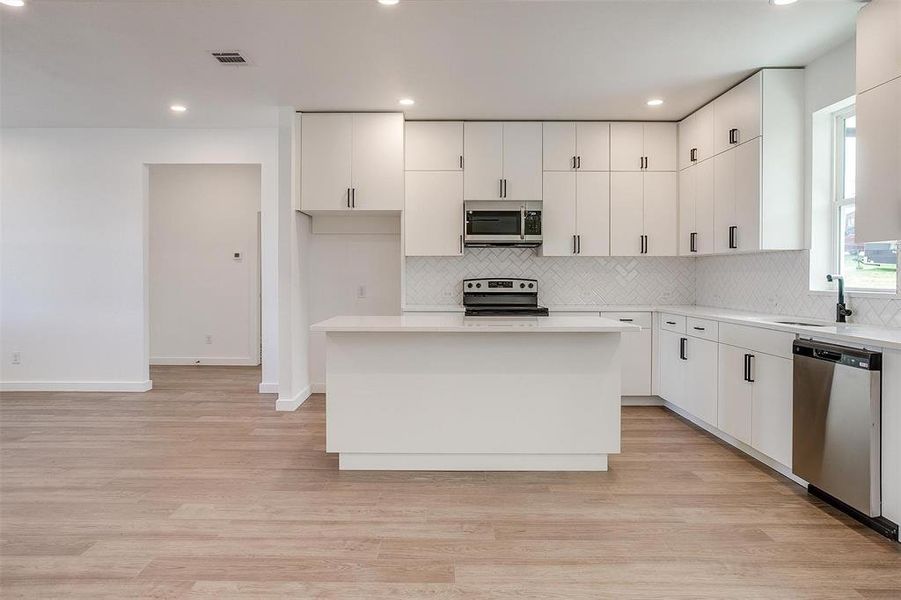 Kitchen featuring stainless steel appliances, decorative backsplash, white cabinets, light countertops, and recessed lighting Kitchen featuring stainless steel appliances, decorative backsplash, white cabinets, light countertops, and recessed lighting