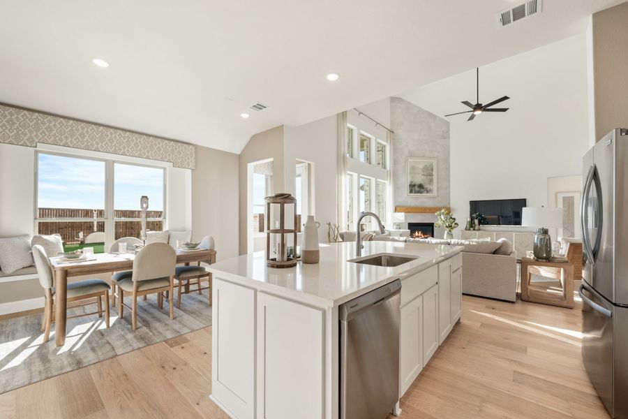 Open-concept kitchen with white island, stainless appliances, and hardwood floors flowing into dining and living areas with fireplace.