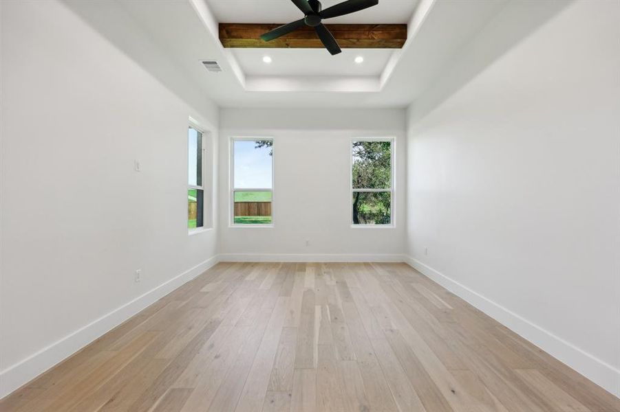 Master bedroom with beamed ceiling, a raised ceiling, light hardwood / wood-style flooring, and ceiling fan