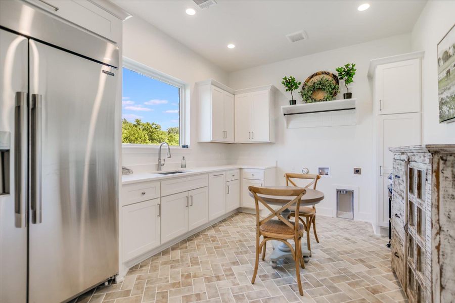 Kitchen featuring high end refrigerator, a sink, white cabinetry, light countertops, and recessed lighting Kitchen featuring high end refrigerator, a sink, white cabinetry, light countertops, and recessed lighting
