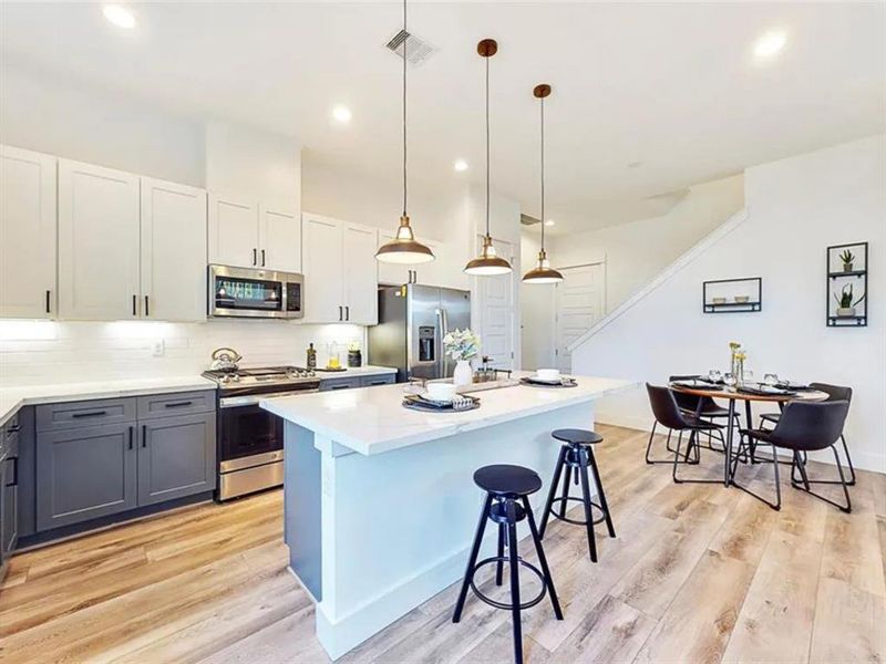 The kitchen is bright and airy, with large windows that let in plenty of natural light. The room is decorated with a few plants and other decorative items, creating a warm and inviting atmosphere. The kitchen is well-equipped, with a microwave, oven, and dishwasher. The overall design of the kitchen is modern and minimalist, with a focus on functionality and clean lines.