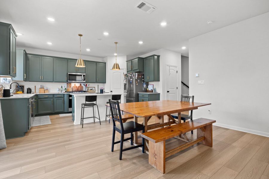 Open-concept kitchen and dining area featuring light wood-finish flooring, recessed lighting, and a white backsplash