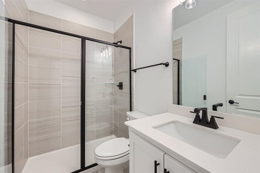 Bathroom featuring a shower with door, toilet, and vanity