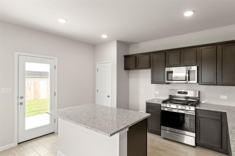Kitchen with appliances with stainless steel finishes, light wood-style flooring, dark brown cabinetry, light stone counters, and recessed lighting