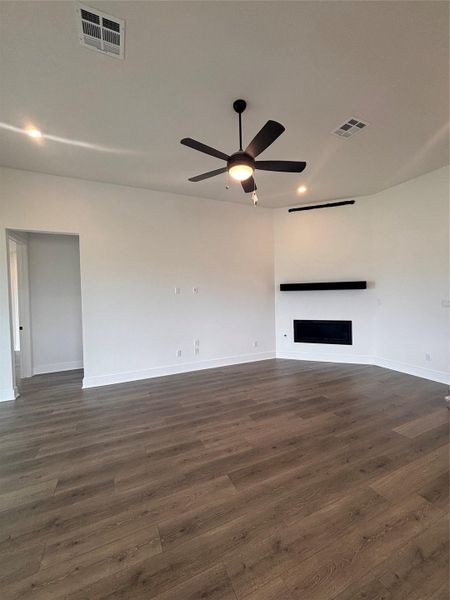 Unfurnished living room featuring baseboards, a ceiling fan, dark wood-style floors, and visible vents Unfurnished living room featuring baseboards, a ceiling fan, dark wood-style floors, and visible vents