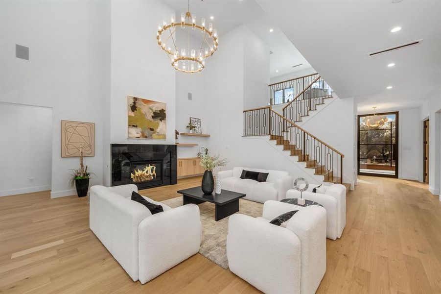 Living room with a chandelier, a tiled fireplace, light wood-type flooring, stairs, and recessed lighting