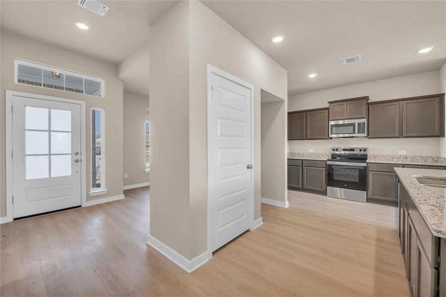 Kitchen with stainless steel appliances, dark brown cabinetry, light stone counters, light wood finished floors, and recessed lighting