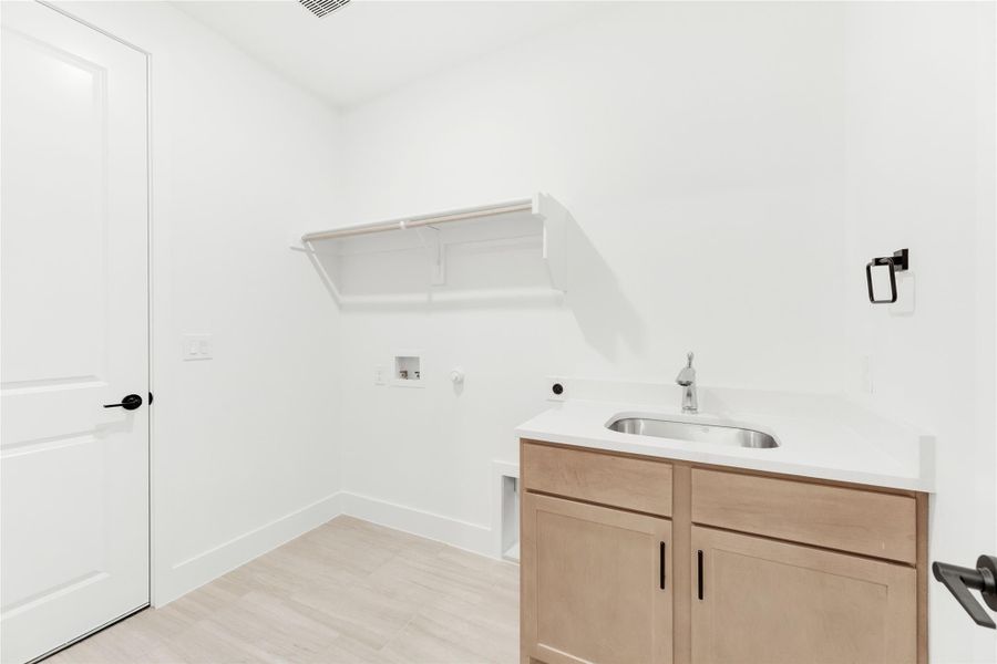 Laundry room with utility sink, wood cabinet, wall shelf, and washer and dryer hookups on light wood floors