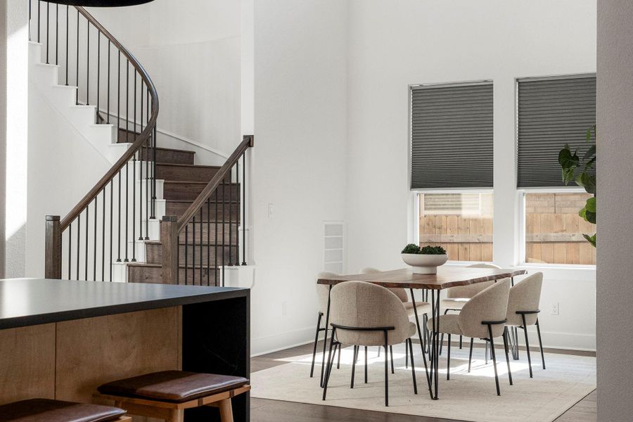 A grand, curving staircase with dark wood and wrought iron balusters complements the dining area's bright windows.