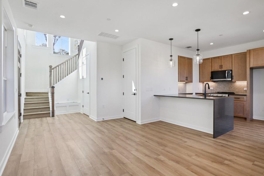 Kitchen featuring pendant lighting, a peninsula, brown cabinetry, stainless steel microwave, and recessed lighting