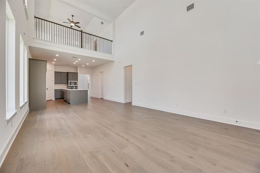 Unfurnished living room featuring light wood-style flooring, a high ceiling, and a ceiling fan Unfurnished living room featuring light wood-style flooring, a high ceiling, and a ceiling fan