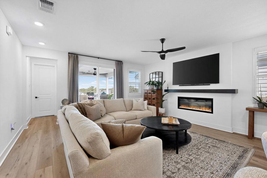 Living room with a ceiling fan, a glass covered fireplace, light wood-type flooring, and recessed lighting