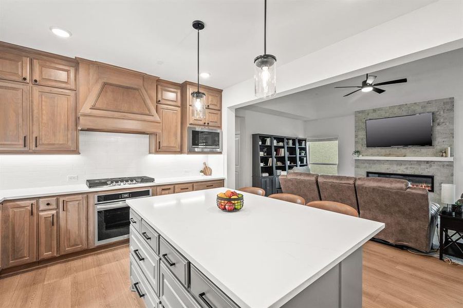 Kitchen with appliances with stainless steel finishes, light wood-style flooring, pendant lighting, open floor plan, and a fireplace Kitchen with appliances with stainless steel finishes, light wood-style flooring, pendant lighting, open floor plan, and a fireplace