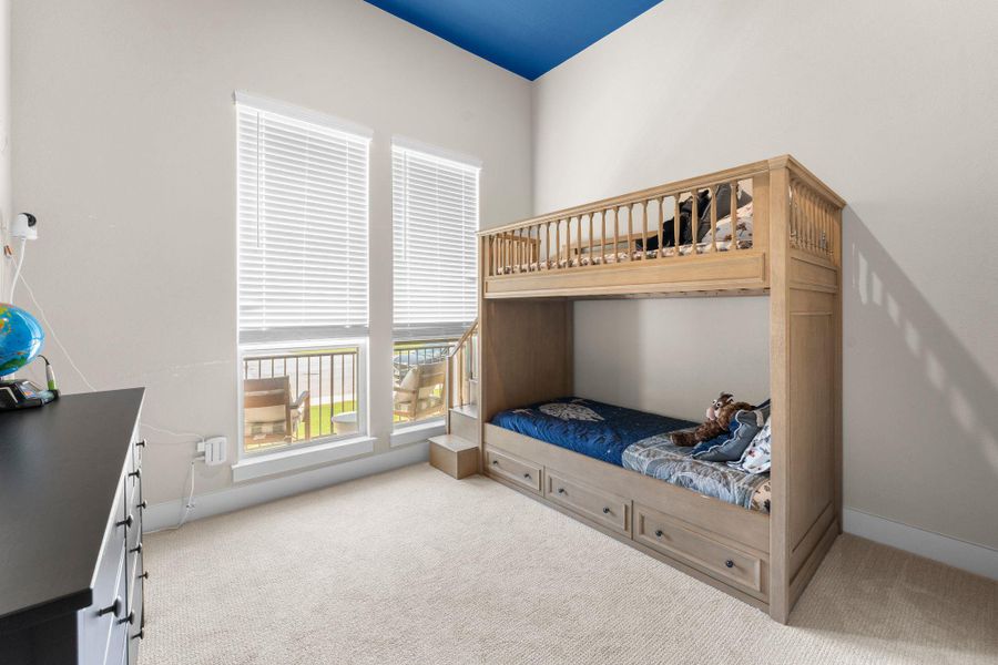 High ceilings with a distinctive blue accent, two large windows providing natural light, white window blinds, and plush carpet flooring