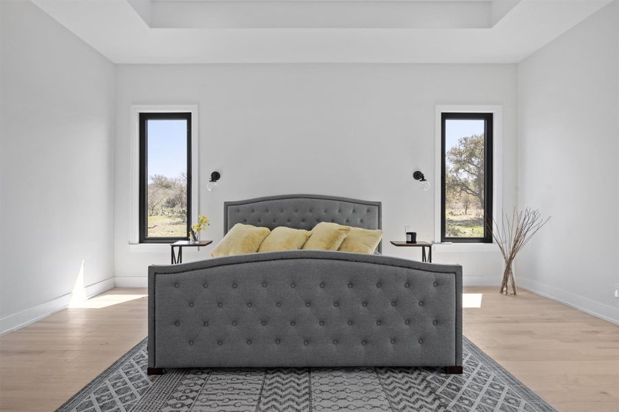 Bedroom featuring a raised ceiling, light wood-style floors, and baseboards