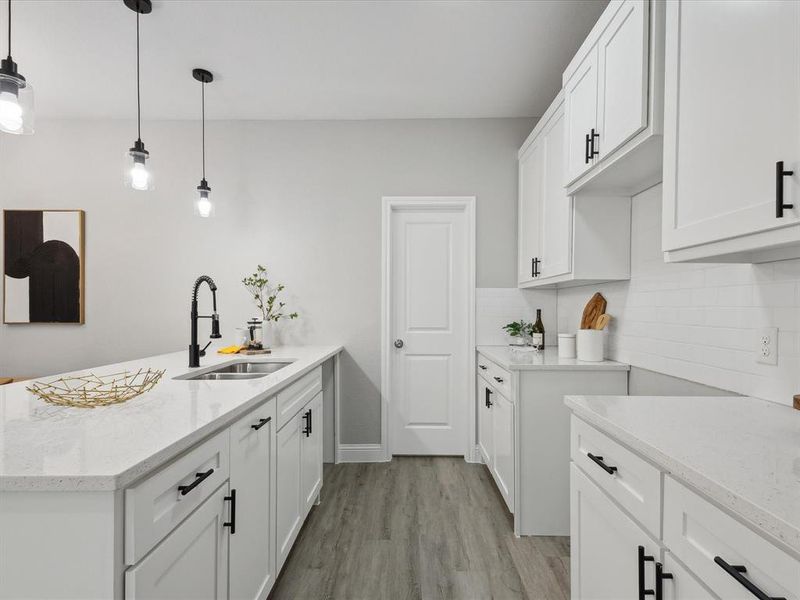 Kitchen with backsplash, sink, hanging light fixtures, white cabinets, and light hardwood / wood-style floors