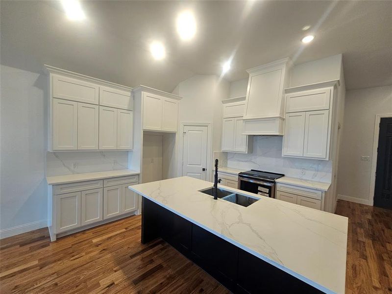 Kitchen with white cabinetry, premium range hood, a center island with sink, and electric range